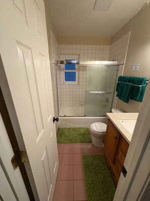 Un baño compacto con cabina de ducha de vidrio, inodoro blanco y una alfombra verde en el suelo.