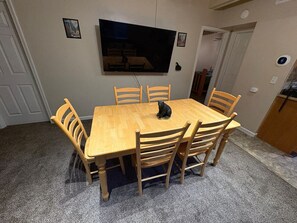 Un comedor con una mesa y sillas de madera, un televisor montado en la pared y una pequeña estatua sobre la mesa.
