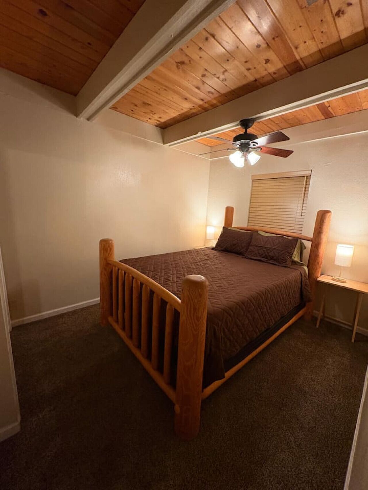 A bedroom with a wooden bed frame, a ceiling fan, and a window with blinds.