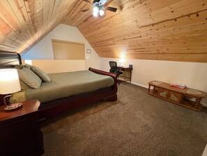 Un dormitorio con techo de madera, cama, escritorio y una mesita.