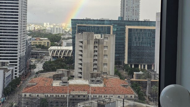 Vista urbana com edifícios modernos, um arco-íris e uma paisagem vista por uma janela.