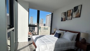 Quarto moderno com uma cama grande, vista para edifícios da cidade e um claraboia.