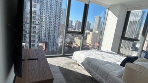 Quarto moderno com cama grande, TV de tela plana e vista para a cidade através de janelas do chão ao teto.