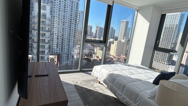 A modern bedroom with a large bed, a flat-screen TV, and a view of a cityscape through floor-to-ceiling windows. - Miami-Brickell Skyline Lux High Rise 2BR-2B -walking distance to KASEYA-BAYSIDE (Miami)