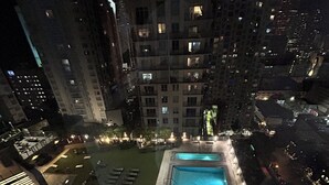 Vista noturna de uma área de piscina no terraço, com piscina retangular, cadeiras de descanso e um pequeno jardim.