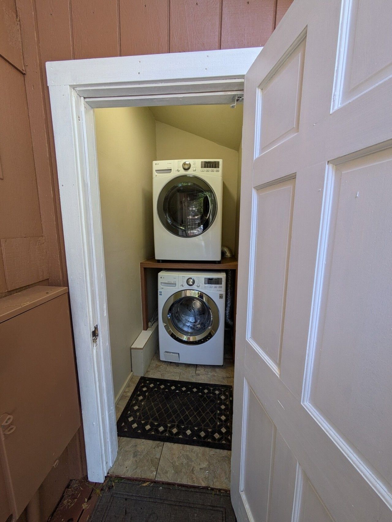 A laundry room with two washing machines, a small shelf, and a doormat.