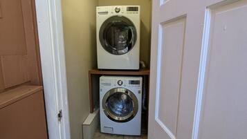 A laundry room with two washing machines, a small shelf, and a doormat.