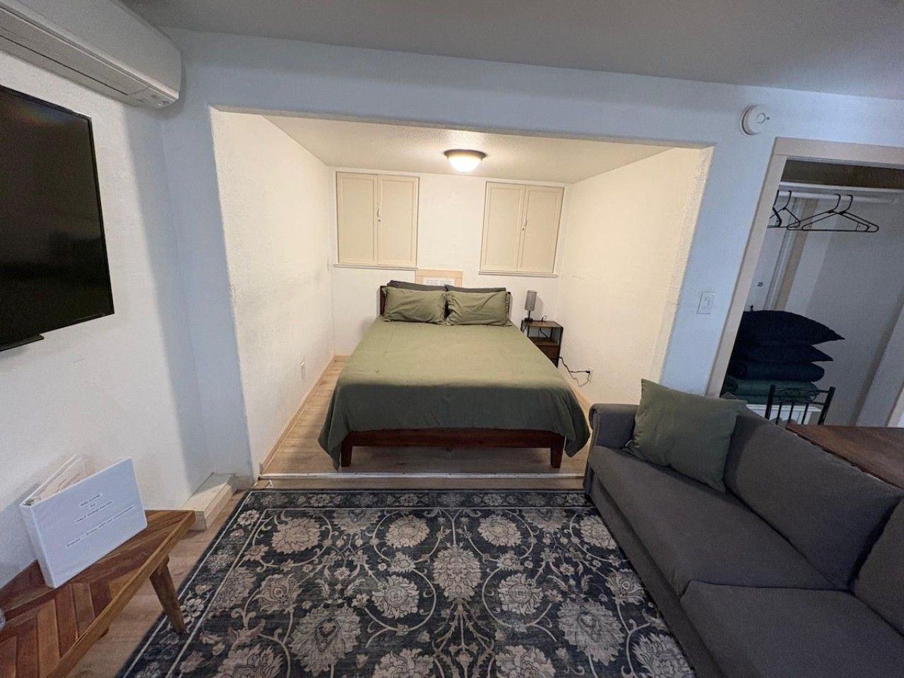 Een slaapkamer met een bed, een bank, een televisie en een kledingkast.