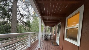 A wooden deck with a white railing, a table with chairs, and a window with blinds.