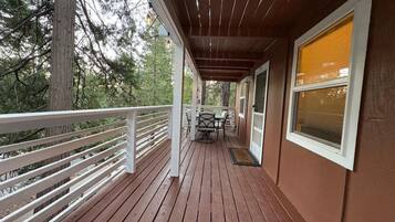A wooden deck with a railing, a table with chairs, and a window with blinds.