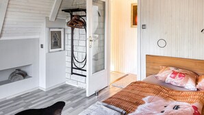 Un dormitorio con una cama de madera, un ventanal de vidrio que da a un baño y un ventanuilla.