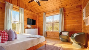 Un dormitorio de cabaña de madera con una cama, un televisor, una silla y una ventana.