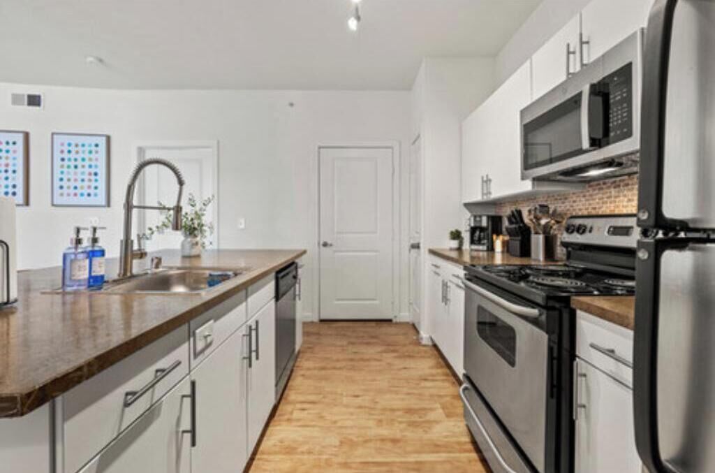 Een moderne keuken met roestvrijstalen apparatuur, een houten aanrecht en een betegelde spatwand.