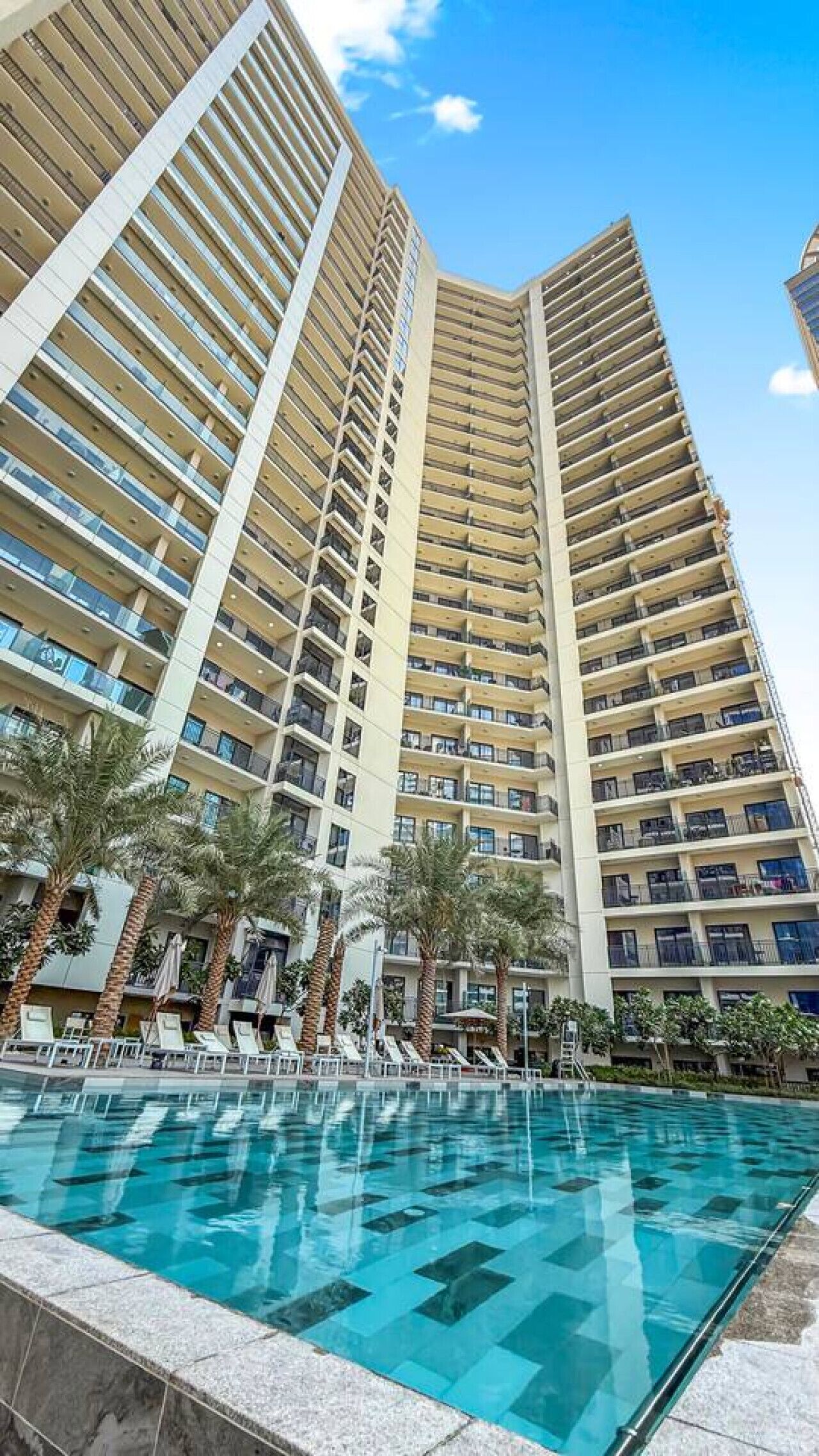 A high-rise hotel with a swimming pool, palm trees, and a clear blue sky.