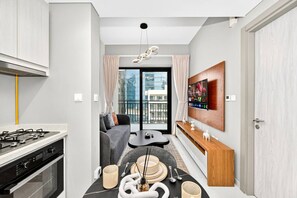 Un apartamento moderno con cocina, comedor y sala de estar. Cuenta con un ventanal grande, un televisor de pantalla plana y un balcón.