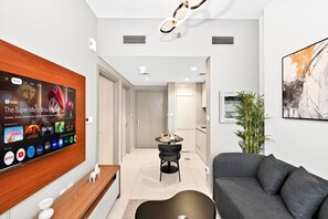 Una sala de estar moderna con un televisor de pantalla plana mostrando una película, un sofá gris, una mesa de centro de madera y una decoración de estilo minimalista.