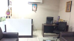 Un espace d’accueil comprenant un comptoir de réception, deux fauteuils de bureau noirs, une table basse en verre et un canapé.