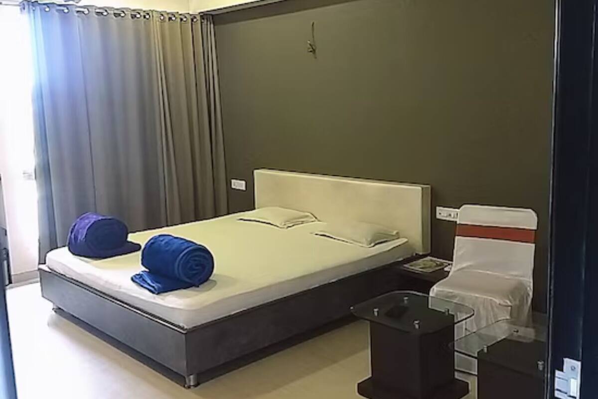Una habitación de hotel con una cama individual, una mesita de noche y una ventana con cortinas.