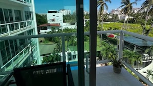 Ein Balkon mit Blick auf ein modernes Gebäude, eine Grünfläche mit Pflanzen und einem wolkenlosen, blauen Himmel.