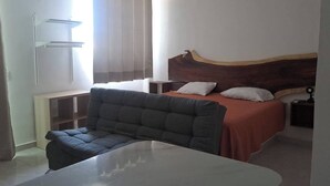 Een slaapkamer met een bed, een sofa, een nachtkastje en een raam met gordijnen.