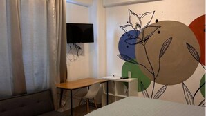 Ein Hotelzimmer mit zwei Betten, einem Schreibtisch, einem Sessel und einem an der Wand befestigten Fernseher.