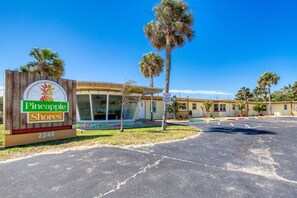Ein Pineapple Shores Motel mit einer großen Schautafel, einem überdachten Außenbereich zum Sitzen und Palmen.