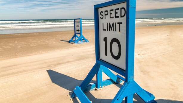 A beach with a speed limit sign indicating a limit of 10. - Pineapple Shores Retro Inn 2 (Daytona Beach)