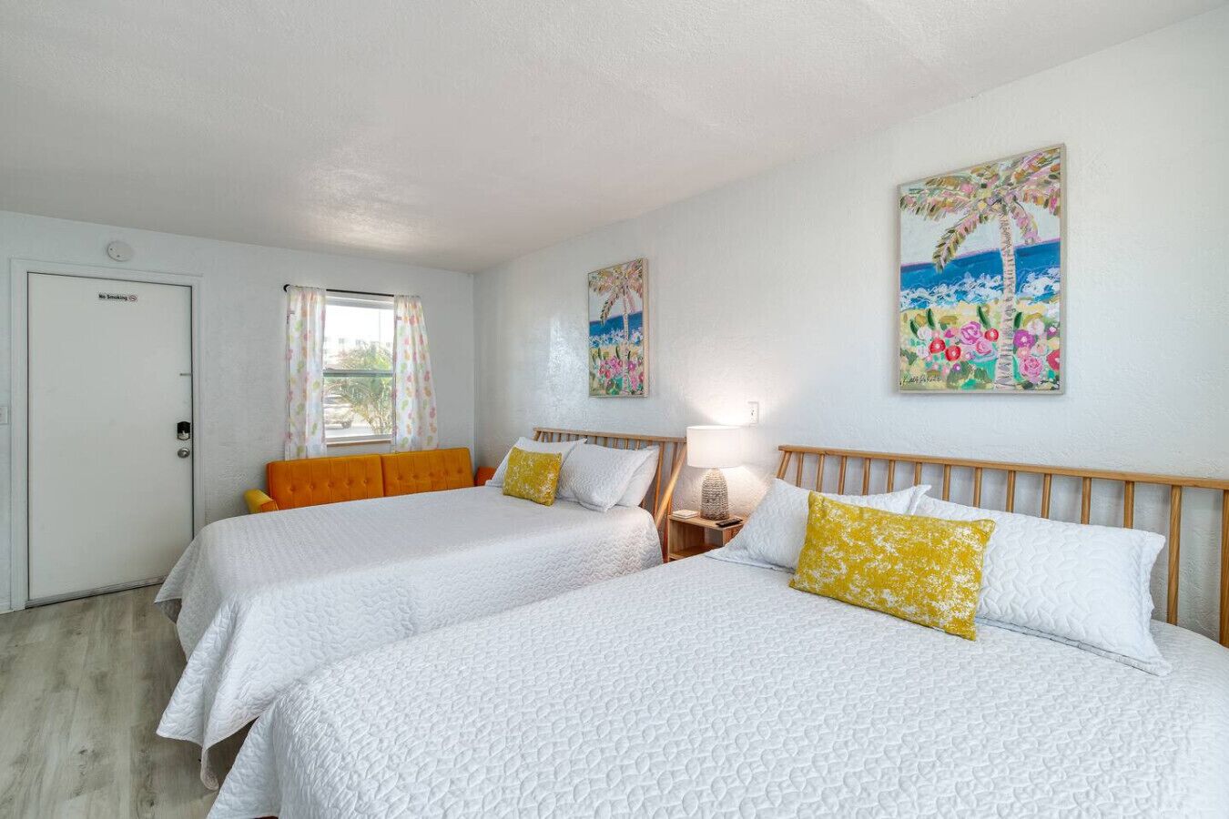 A hotel room with two beds, a wooden headboard, a nightstand with a lamp, and a door with a 'No Smoking' sign.