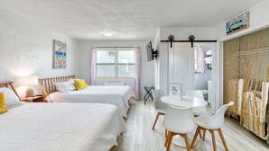 A hotel room with two beds, a round table with chairs, a window with curtains, and a wall-mounted TV. - Pineapple Shores Retro Inn 2 (Daytona Beach)