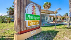 A sign for 'Pineapple Shores' with a wooden background and a logo featuring a pineapple and palm trees. - Pineapple Shores Retro Inn 2 (Daytona Beach)