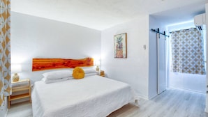 A bedroom with a large bed, a wooden headboard, a painting, and a shower area with patterned curtains. - Pineapple Shores Retro Inn 7 (Daytona Beach)