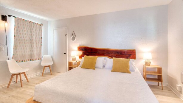 Ein Hotelzimmer mit einem großen Bett, zwei Nachttischen mit Lampen, einem Sessel und einem Vorhang mit Muster.