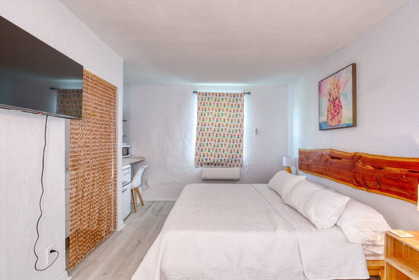 A bedroom with a bed, a desk, a chair, a TV, and a window with curtains.