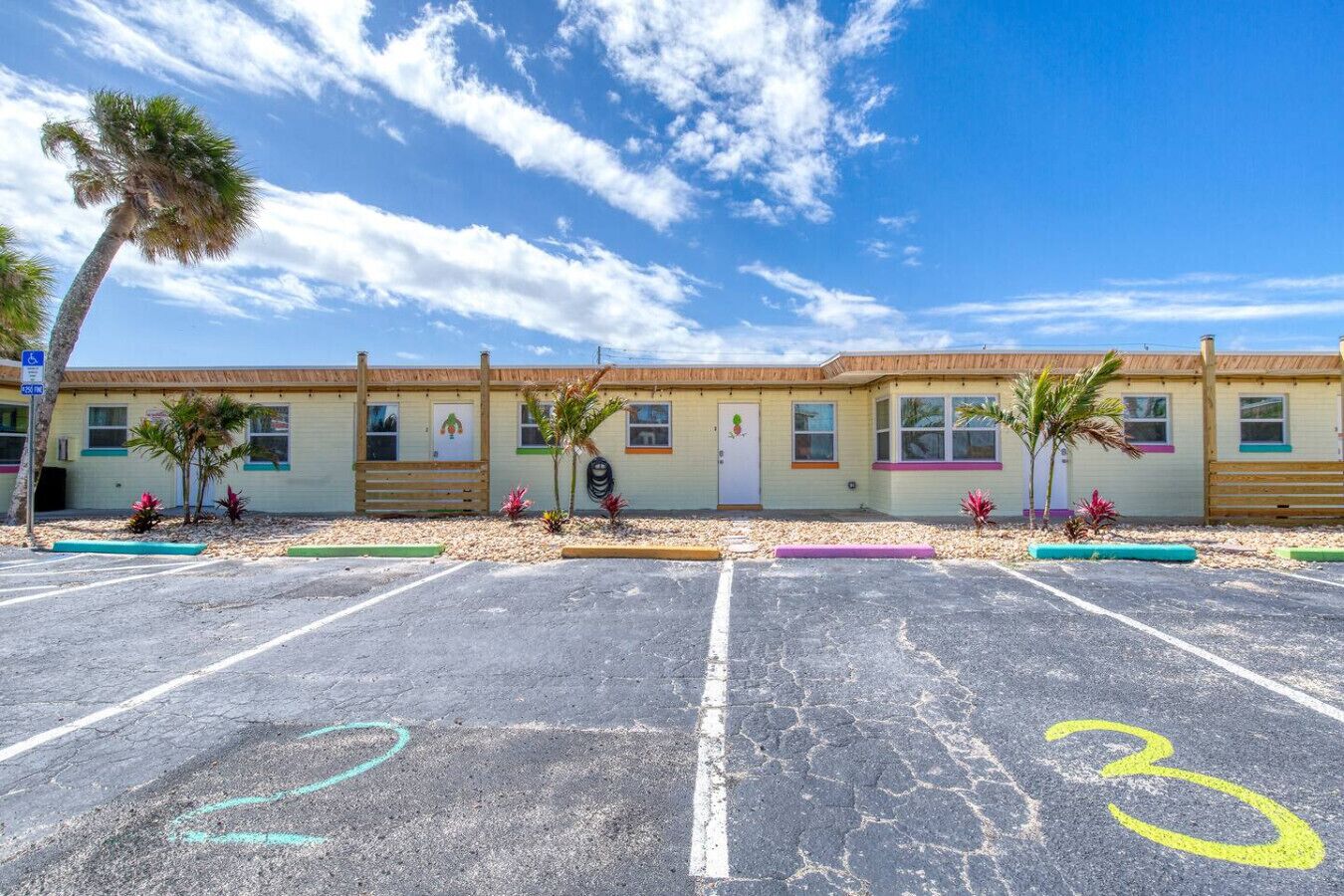 Un motel con una fila de habitaciones, un estacionamiento y una palmera.