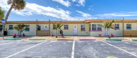 Un motel con una fila de habitaciones, un estacionamiento y una palmera.