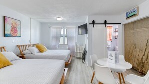 Une chambre d’hôtel avec deux lits, une télévision, une petite table avec des chaises et une fenêtre avec des rideaux.
