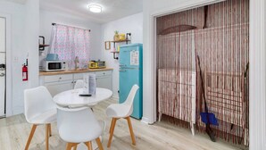 A compact kitchen with white cabinets, a microwave, a blue refrigerator, and a dining area with white chairs. - Pineapple Shores Retro Inn 5 (Daytona Beach)