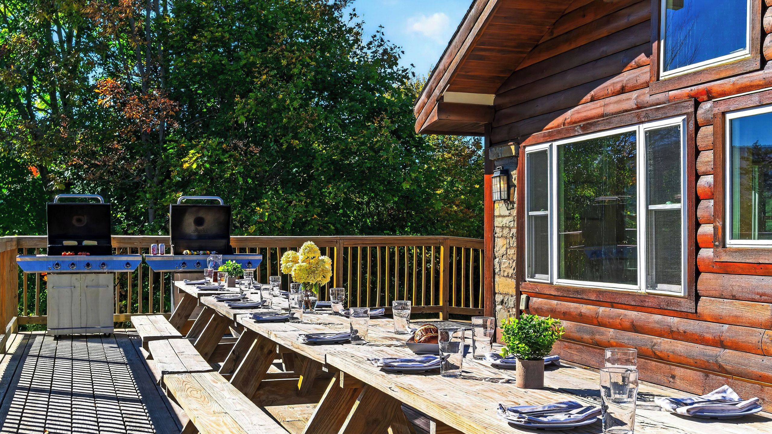 An outdoor dining area with a wooden deck, a grill, and a table set for a meal.