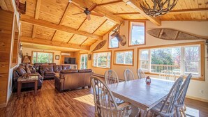 A spacious living room with a large wooden ceiling, a fireplace, and a dining area with a table and chairs. - Mins to Hunter Mountain Sleeps 36 Pool, Spa, Games & Bar Cozy Peaks Lodge by Avantstay (Tannersville)