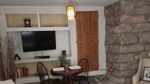 Una sala de estar con una pared de piedra, una mesa de comedor con sillas, un televisor y una chimenea.