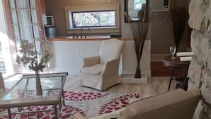 Un salón con sofá, sillón y una mesa de centro de cristal. Un tapete estampado rojo cubre el suelo.