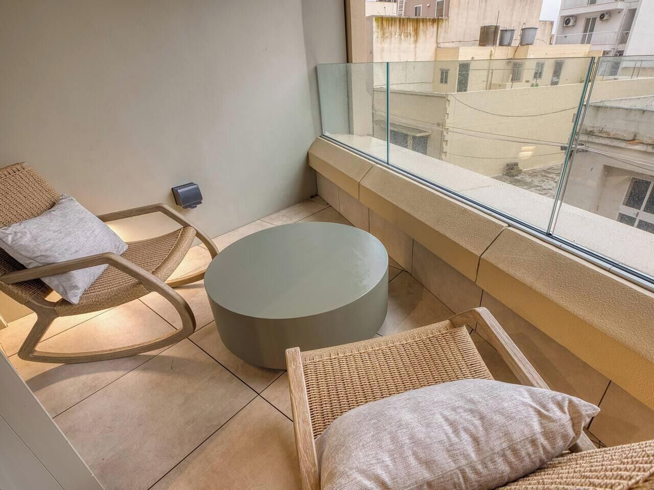 A balcony with wicker furniture, a round ottoman, and a glass railing.