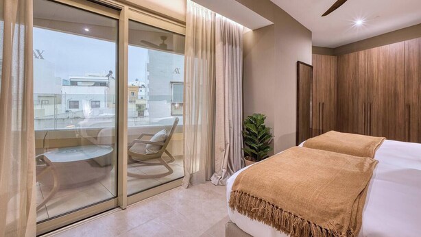 A modern hotel room with a large bed, a ceiling fan, a balcony with a chair, and a view of the city. - Elegant 2BR Retreat with Balcony & Fast Wi-Fi (Rabat)