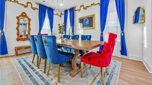 Une salle à manger avec une table en bois, des chaises recouvertes d’un tissu bleu et rouge, et des rideaux bleus.