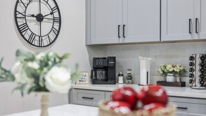 Une cuisine avec des meubles de couleur grise, une machine à café et une horloge au mur.