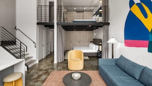 Ett modernt rum i loftstil med en säng placerad på en övre våning, en soffa, en fåtölj, ett soffbord och en trappa.
