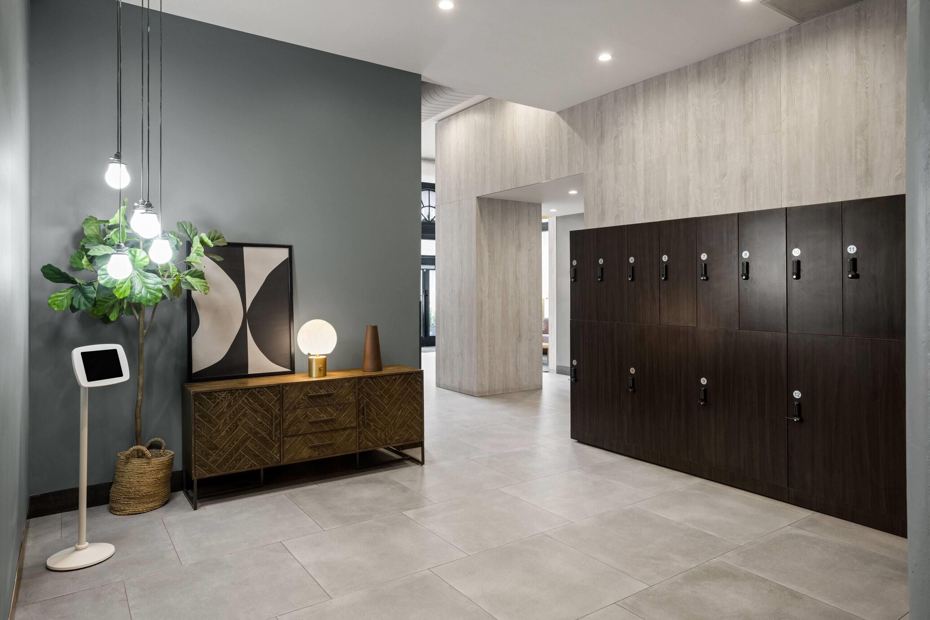 A modern lobby with a dark wooden wardrobe, a herringbone-patterned cabinet, a hanging light fixture, and a large abstract artwork.