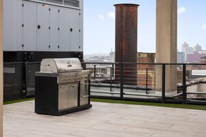 En takterrass med en grill, en stor industriell luftkonditioneringsanläggning och utsikt över stadsbilden.