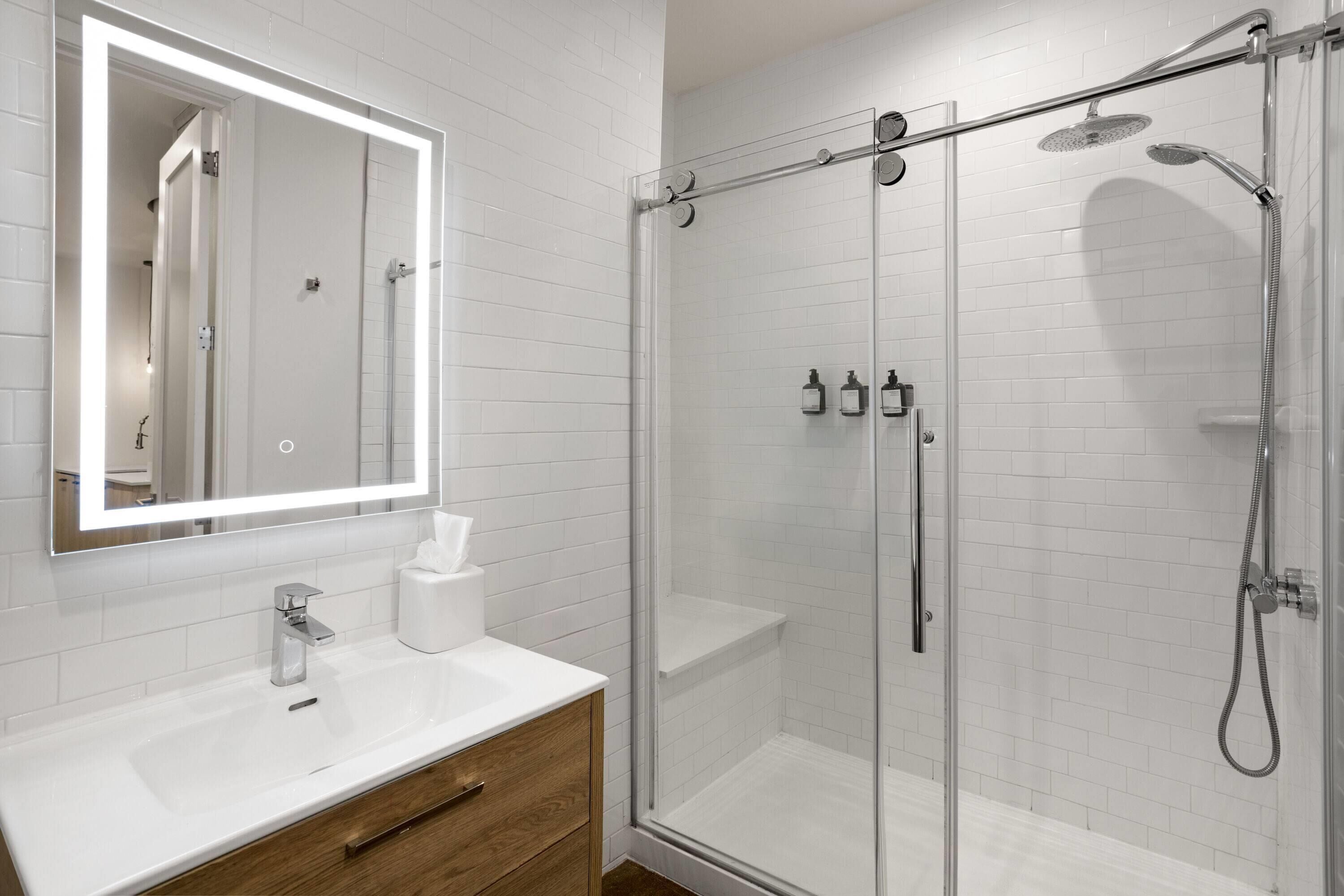 A modern bathroom with a glass-enclosed shower, a white sink, and a mirror with built-in lighting.