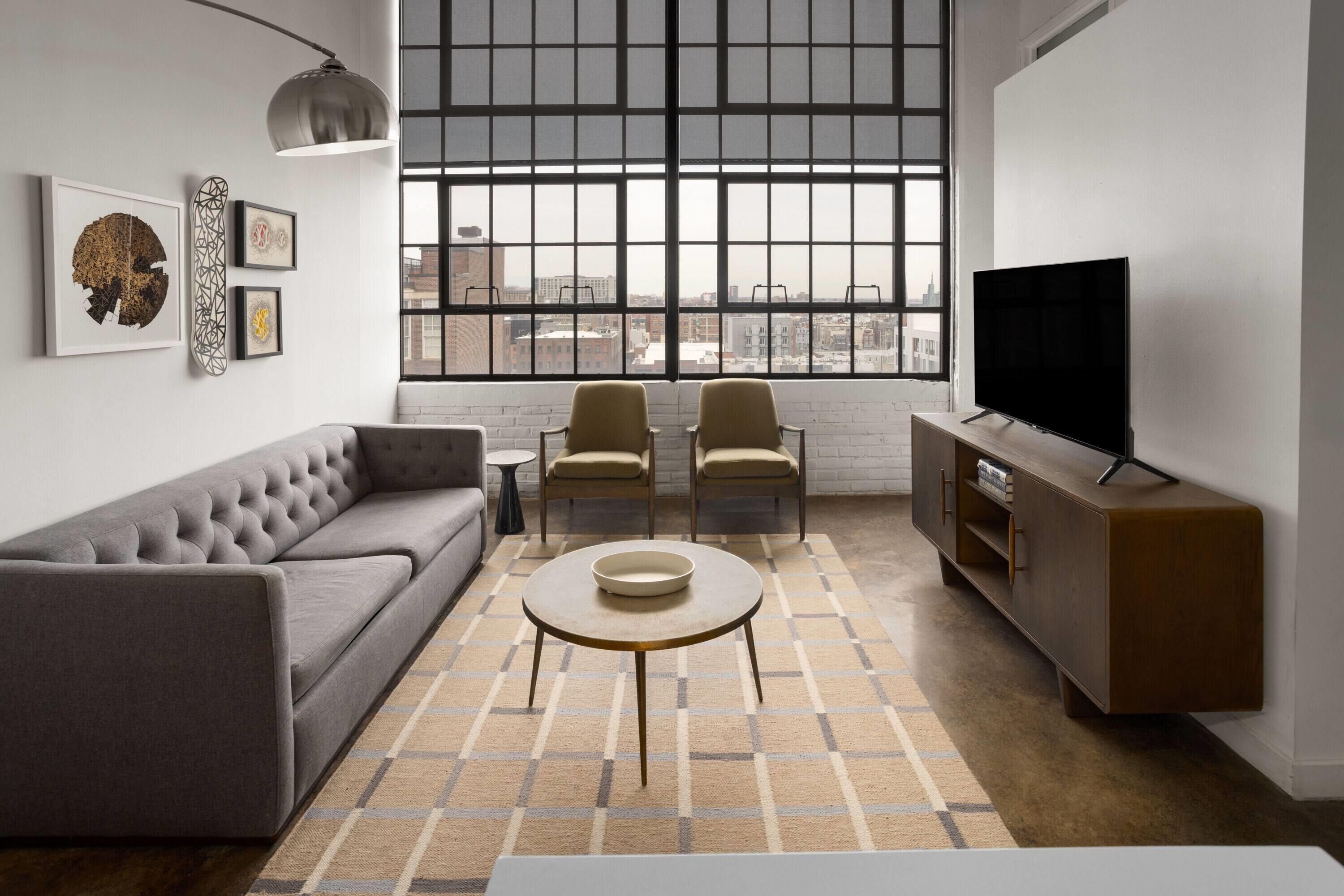 A modern living room with a sofa, two chairs, a coffee table, a TV, and artwork on the wall.